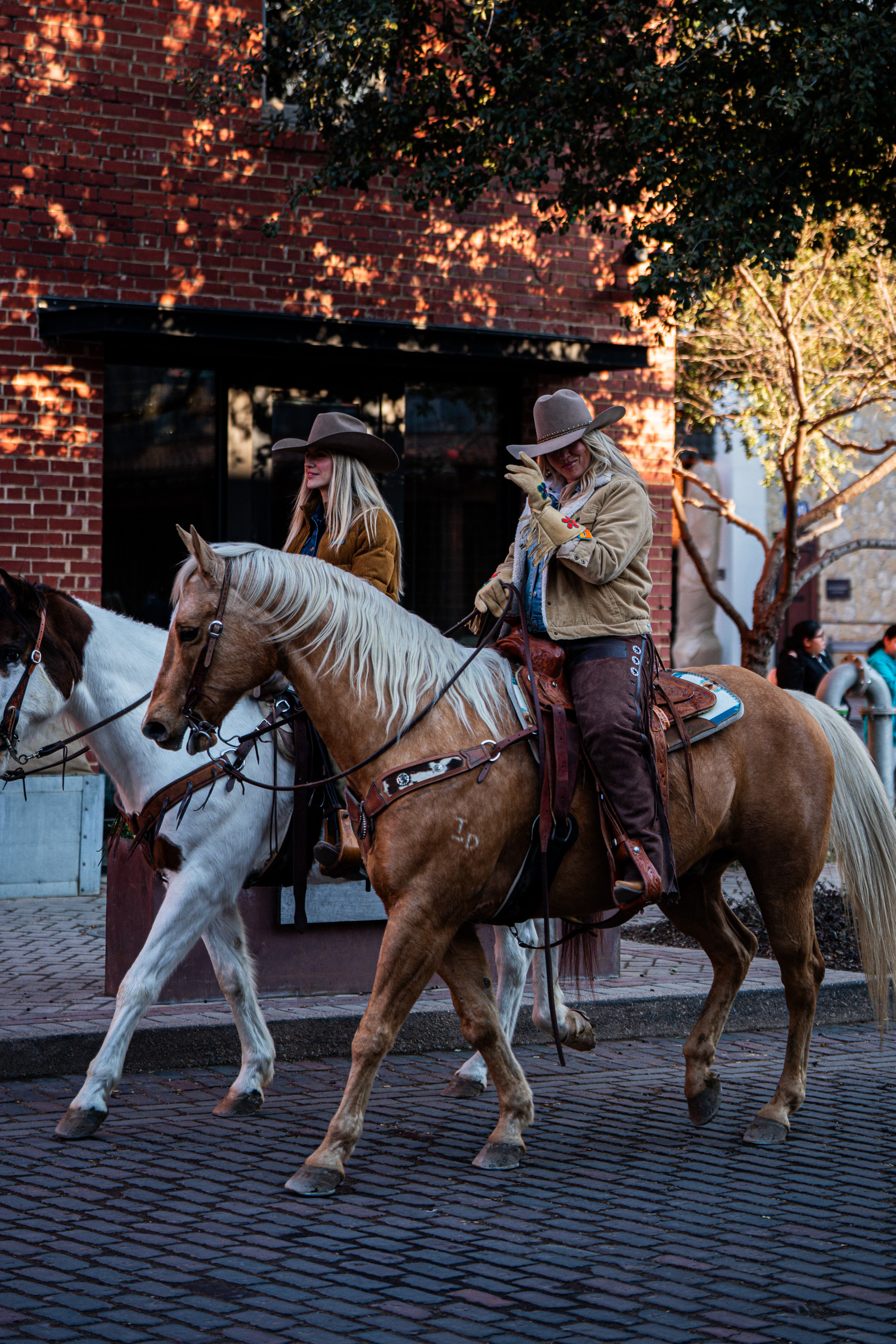 Two riders on horseback passing a brick wall
