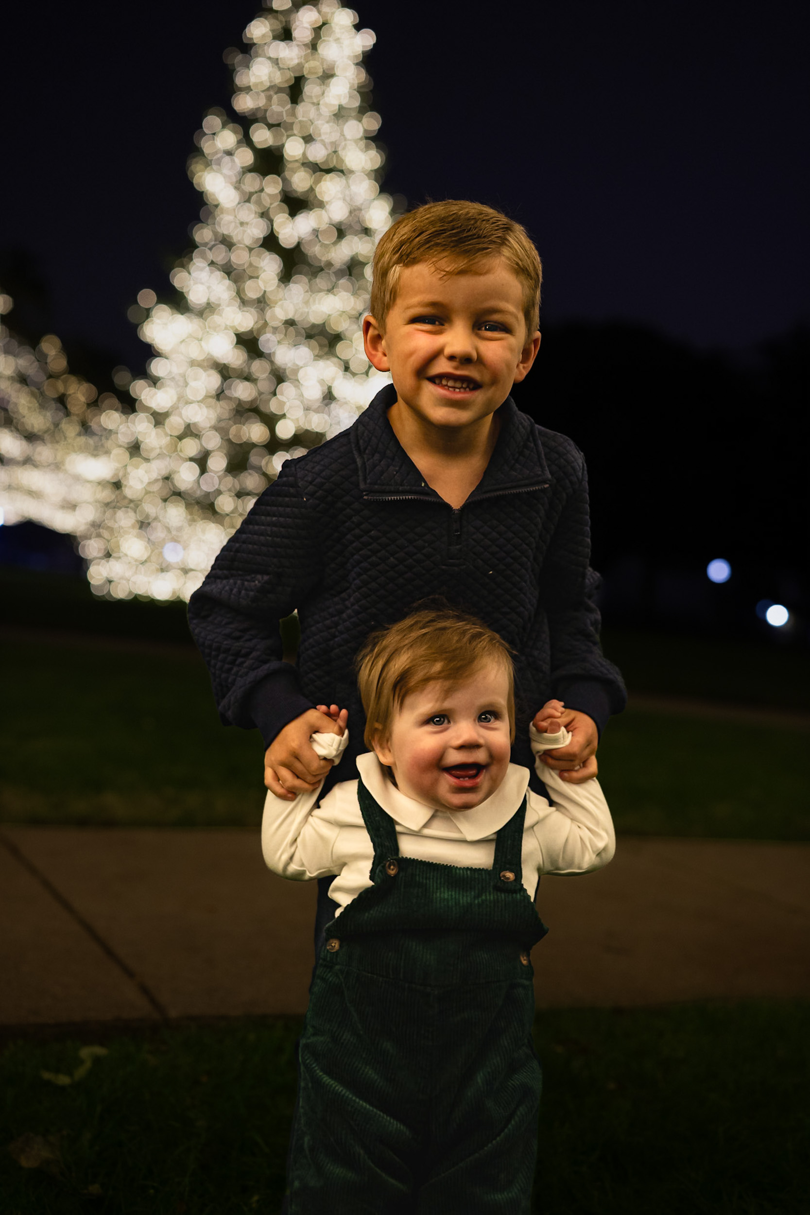 Two brothers by Christmas tree lights at night